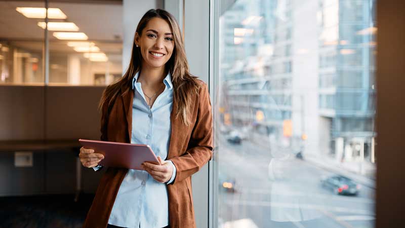 woman with ipad leaned against a window overlooking a city street 